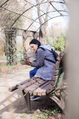Fototapeta premium Portrait of beautiful brunette girl in plaid coat sits on a bench in the park
