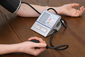 Woman checking blood pressure at wooden table indoors, closeup