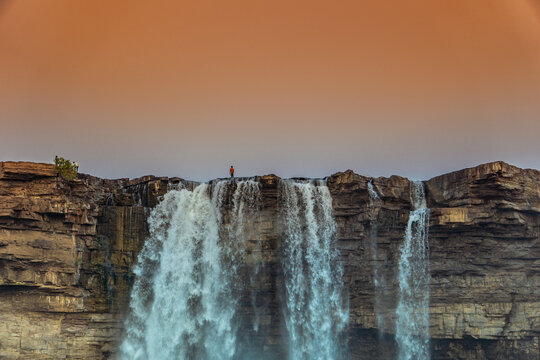 Breathtaking landscape of a man standing on the top of a waterfall cliff