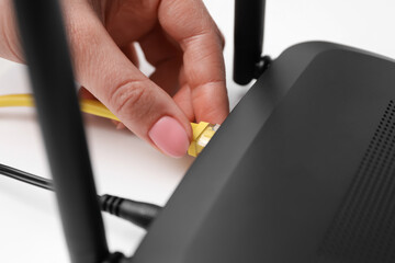 Woman connecting cable to router at white table, closeup. Wireless internet communication