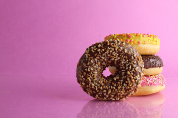 Sweet still life donut berliner close-up at the back lie a stack of three doughnut chocolate pink yellow on a bright pink fuchsia background with a place for text for a cafe for tablecloths for glue