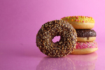 Sweet still life donut berliner close-up at the back lie a stack of three doughnut chocolate pink yellow on a bright pink fuchsia background with a place for text for a cafe for tablecloths for glue