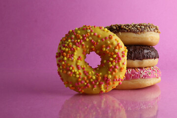 Sweet still life donut berliner close-up at the back lie a stack of three doughnut chocolate pink yellow on a bright pink fuchsia background with a place for text for a cafe for tablecloths for glue