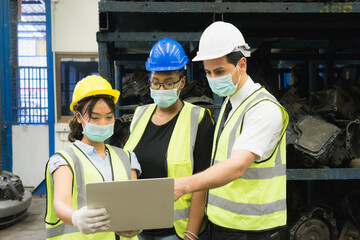 Men and woman work together, wear safety facemask and using laptop. Caucasian engineer men, black woman, Asian woman wear facemask and using laptop in factory-warehouse