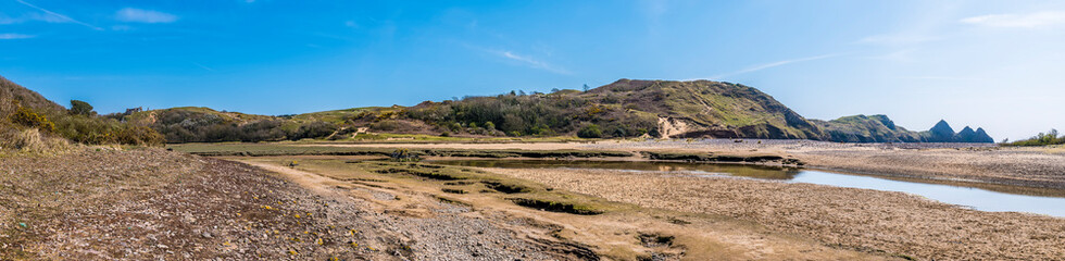 A panorama view across the stream and the beach at Three Cliffs Bay, Gower Peninsula, Swansea, South Wales on a sunny day
