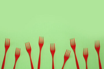 Plastic forks on green background, flat lay. Space for text
