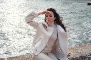 A woman in beige clothing enjoying the view of the sea on a warm, windy day.