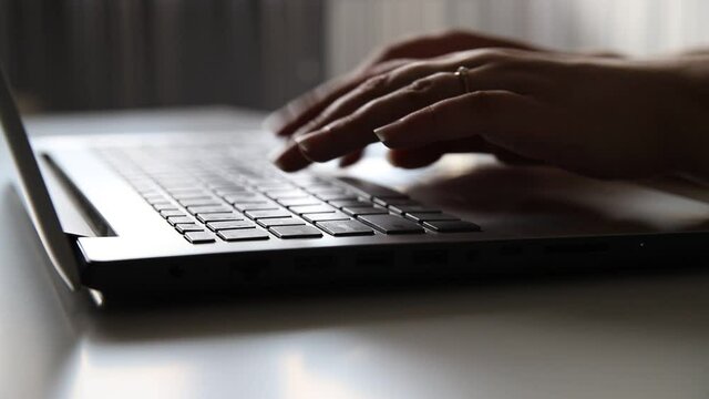 Female hands of a business woman using text input on the keyboard of a silver gray laptop, sitting at a home or office table. Working online concept, close-up 