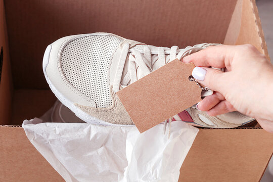 Female Hand Puting Sport Shoes With Mockup Label In Opened Cardboard Box