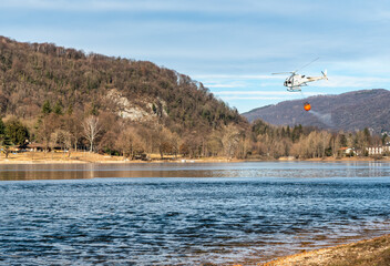 The helicopter load water from Lake Ghirla to extinguish the mountain flames in Valganna, Italy. The fight against forest fires.