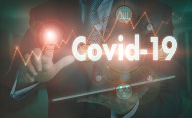 A businessman operating a computer display with a Covid-19 business word concept on it.