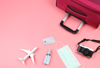  flat lay of traveling accessories with face mask and alcohol spray  on pink background.protection from corona virus or COVID-19 during traveling concept.