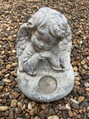 Fototapeta premium Little cute cupid angel sculpture on river gravel background in the english garden.