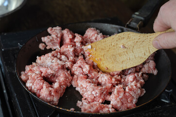 A man is frying minced meat in a pan.