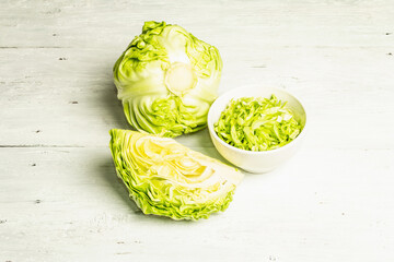 Obraz premium Fresh young shredded cabbage, whole head and cut piece on white wooden background