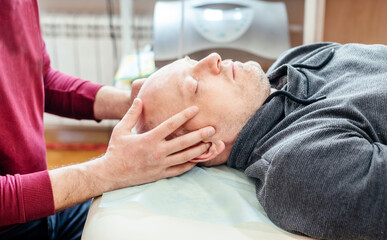 Obraz na płótnie Canvas Male patient receiving cranial sacral therapy, lying on the massage table in CST osteopathic clinic, osteopathy and manual therapy