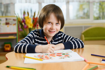 Smiling preschool boy draws in his notebook