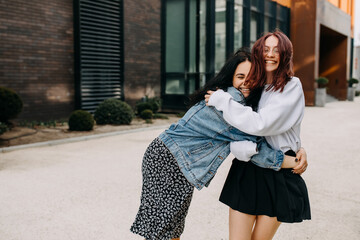 Two young happy women walking down the street, hugging and laughing. Best friends concept.