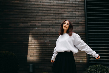 Young woman student wearing eyeglasses, white sweatshirt and black skirt on city buildings...