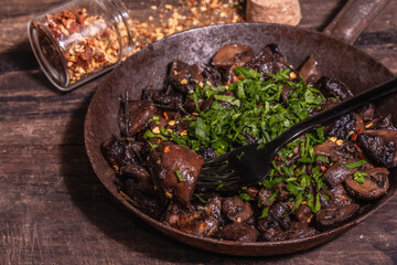 Fried royal champignons in an old cast-iron skillet with trendy hard light, dark shadow