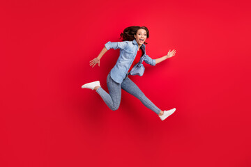 Photo of adorable excited young woman wear jeans shirt smiling jumping high hurrying isolated red color background