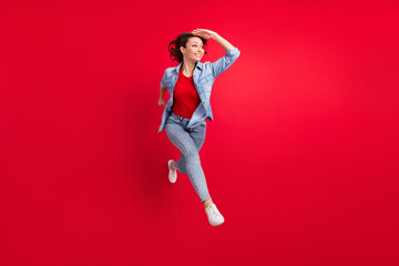 Full length body size photo of cheerful girl jumping up running looking far blank space isolated vivid red color background