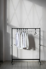 White shirts hanging on the rail of clothes rack in a modern light minimalist interior.