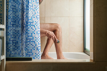 portrait of an intimate moment of an unrecognizable man with beard shaving his leg in the bathroom...