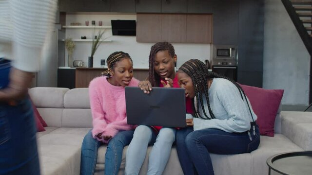 Smiling mischievous cute african american teenage girls with braided hair networking on laptop, watching online forbidden content while strict attractive mother caught them in misbehavior at home.