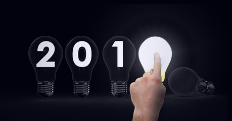 Composition of 201 written on light bulbs with finger touching lit light bulb on black background
