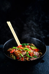 delicious noodles with tuna and vegetables on a dark stone background with hot steam