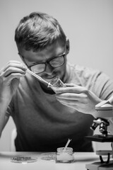 young bearded biologist with glasses drops reagent on plant leaf Black and white photography. laboratory concept. guy student conducts research in lab.