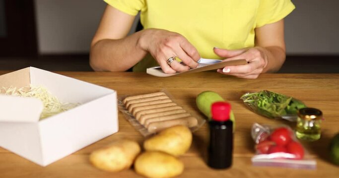 Woman reading a recipe from a meal kit box near of fresh ingredients order from a meal kit company, delivered, cooking at home.