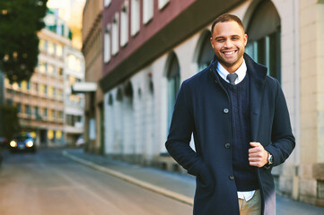 Urban portrait of handsome African American male model, wearing blue coat, posing outside