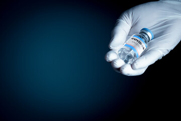 The man's right hand, wearing medical gloves, holds a bottle with the message covid-19 vaccine in his paws. Blurred background