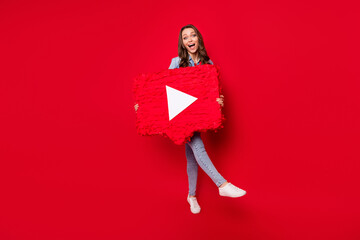 Photo of adorable excited young lady dressed denim outfit walking holding video player button smiling isolated red color background