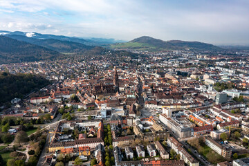 Fototapeta na wymiar Luftaufnahme von Freiburg im Breisgau, das Münster mit speziellem gotischem turm im Vordergrund und schneebedeckte Berge im Hintergrund, Baden Wuertenberg, Deutschland