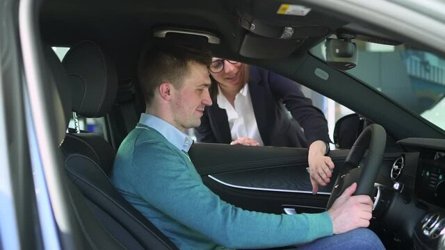 Sales manager car agent tell man client about steering wheel as he sit on sit in new auto Spbas