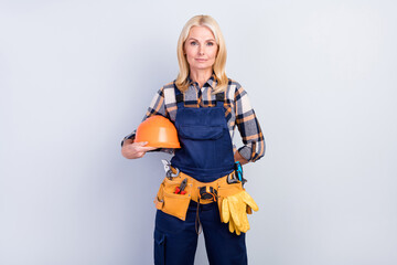 Photo of charming confident mature handywoman workwear holding hard hat isolated grey color background