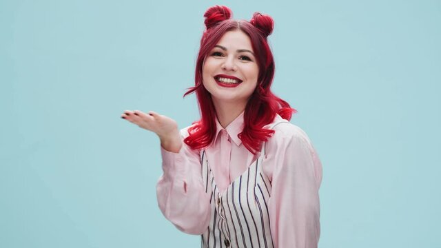 A lovely woman with red lips is sending an air-kiss to the camera standing isolated over a blue wall in the studio