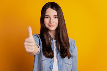 Gorgeous young girl showing thumb up on yellow background