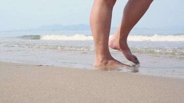 Female feet enter the waves of the sea on the beach