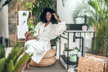 Beautiful dark-skinned woman in na bath robe looking enjoyed and pleased