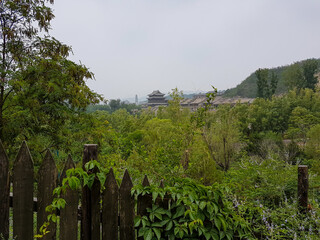 A distant view on the temple complex in Beijing, China. There is a five storied pagoda towering above the horizon. Thick bamboo forest overgrowing the area. A wooden fence in the front. Air pollution