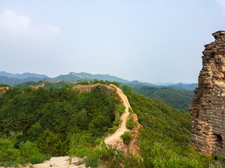 A panoramic view on an unrenewed Gubeikou part of Great Wall of China. The wall is spreading on tops of mountains. Many watchtowers on the peaks. Dense forest around it. World wonder. Tradition