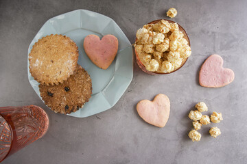 a blue plate of cookies, next to a glass filled with popcorn. several grains of popcorn and pink heart-shaped cookies lie next to a plate and a glass. photo above