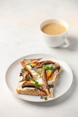 Toast with cream cheese, sprats and eggs in a plate on the table. Breakfast