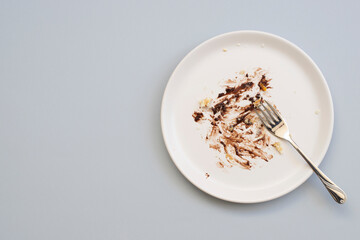 Dirty plate with cake leftovers and fork on gray background, top view