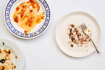 Dirty plates with food leftovers and fork on white background, top view