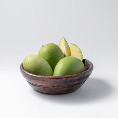 natural raw or green mangos or aam in a wooden bowl with green mango leaves on a white background useful for packaging or editorial purpose